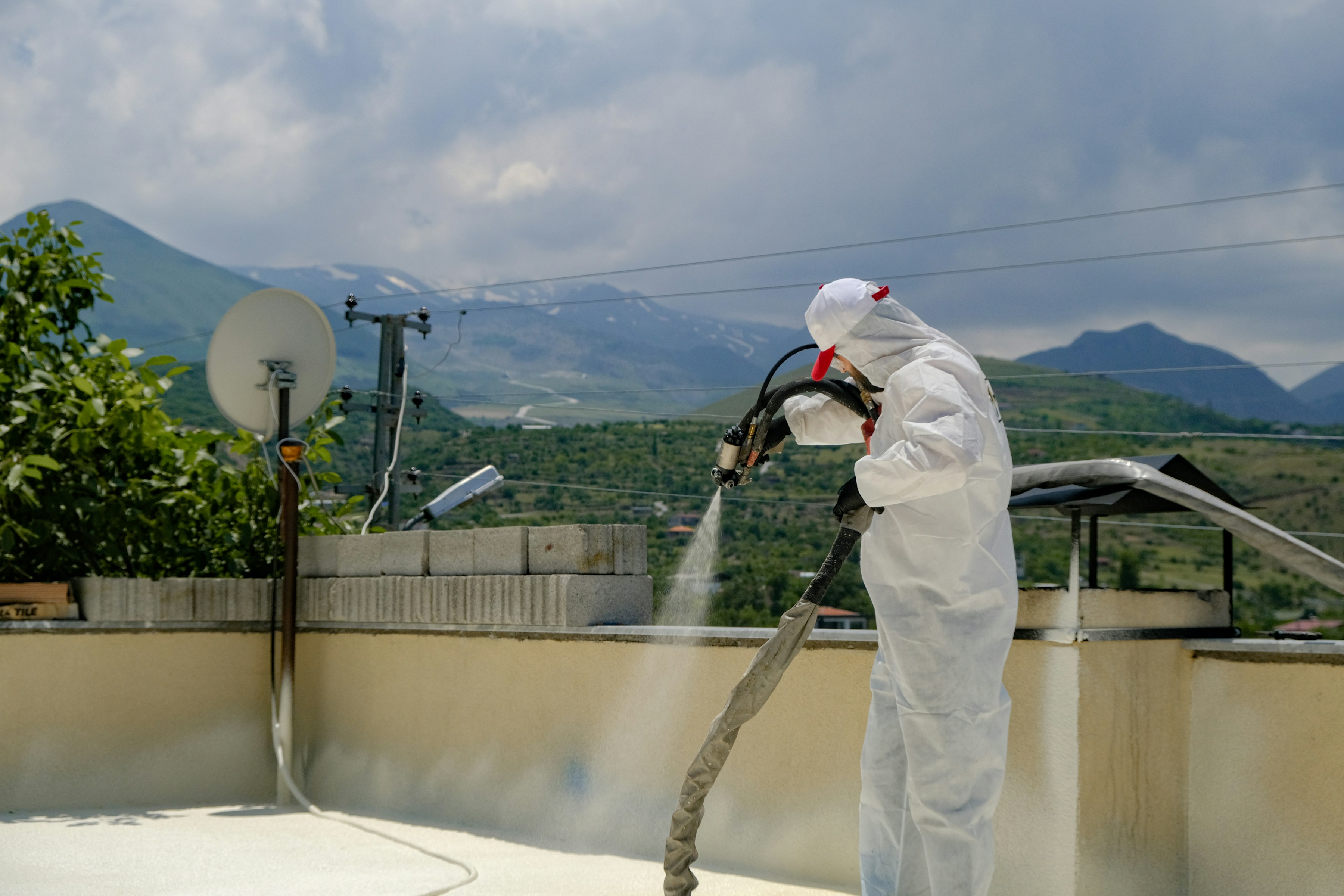 Applicator spraying polyurethane foam on a rooftop, mountains in the distance