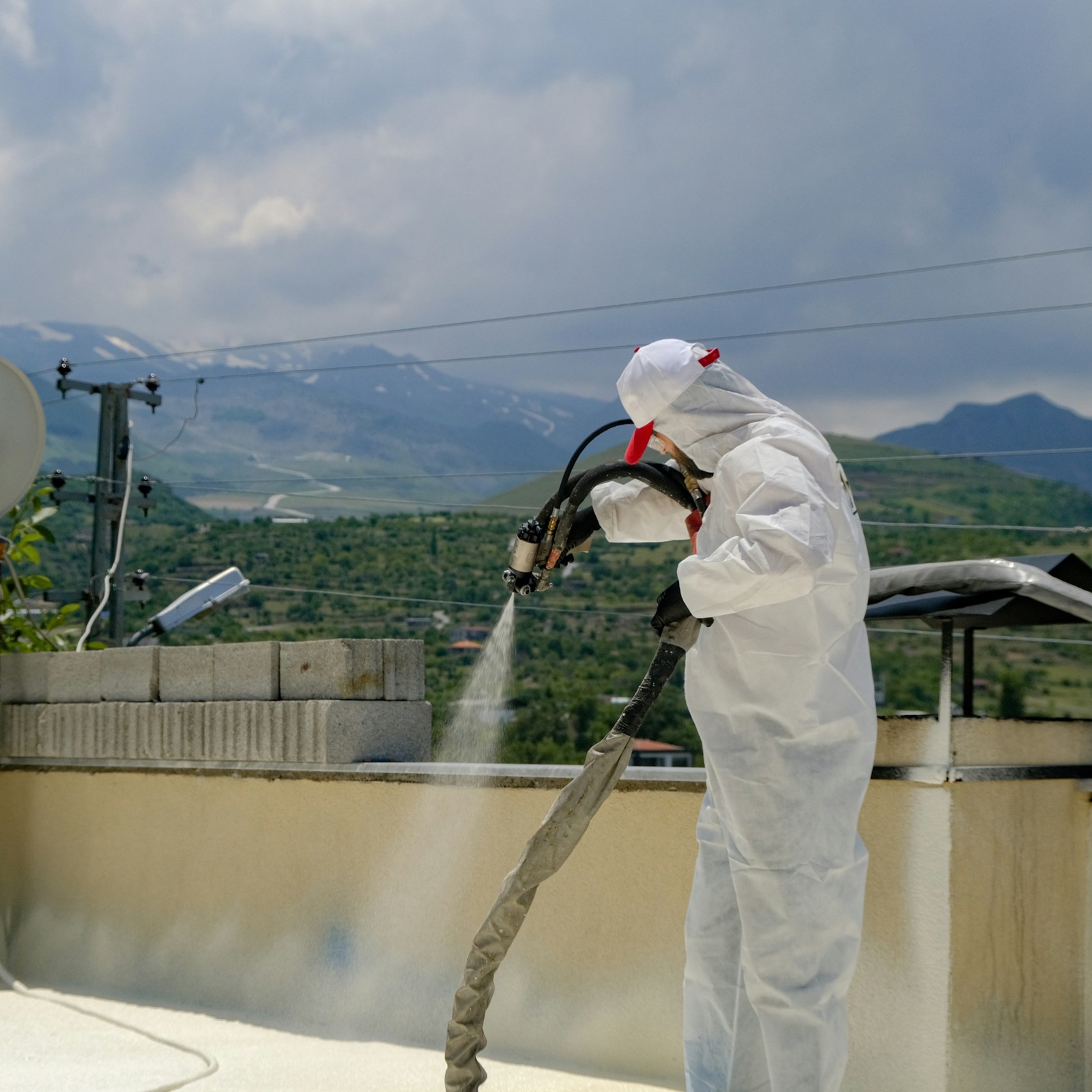 Applicator in protective coverall spray-applying polyurethane foam on a rooftop