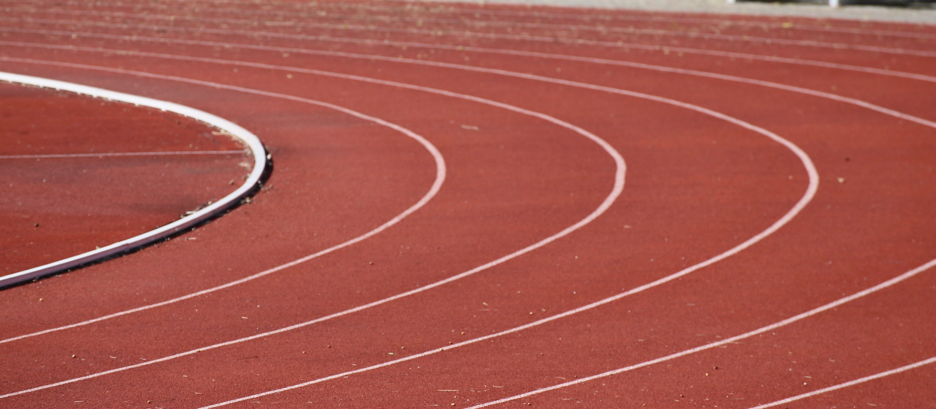 Wide view of a red synthetic running track at an outdoor stadium, curved white lane lines sweeping through the bend