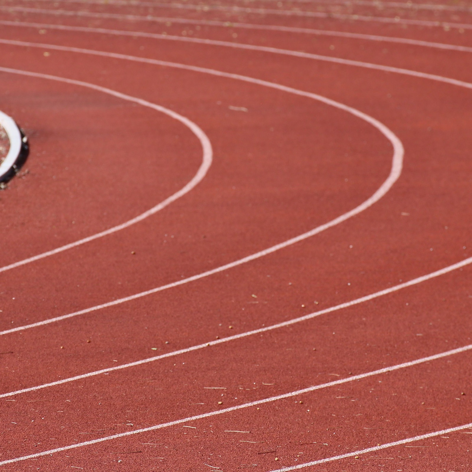 Red synthetic athletics track with curved white lane lines at an outdoor stadium