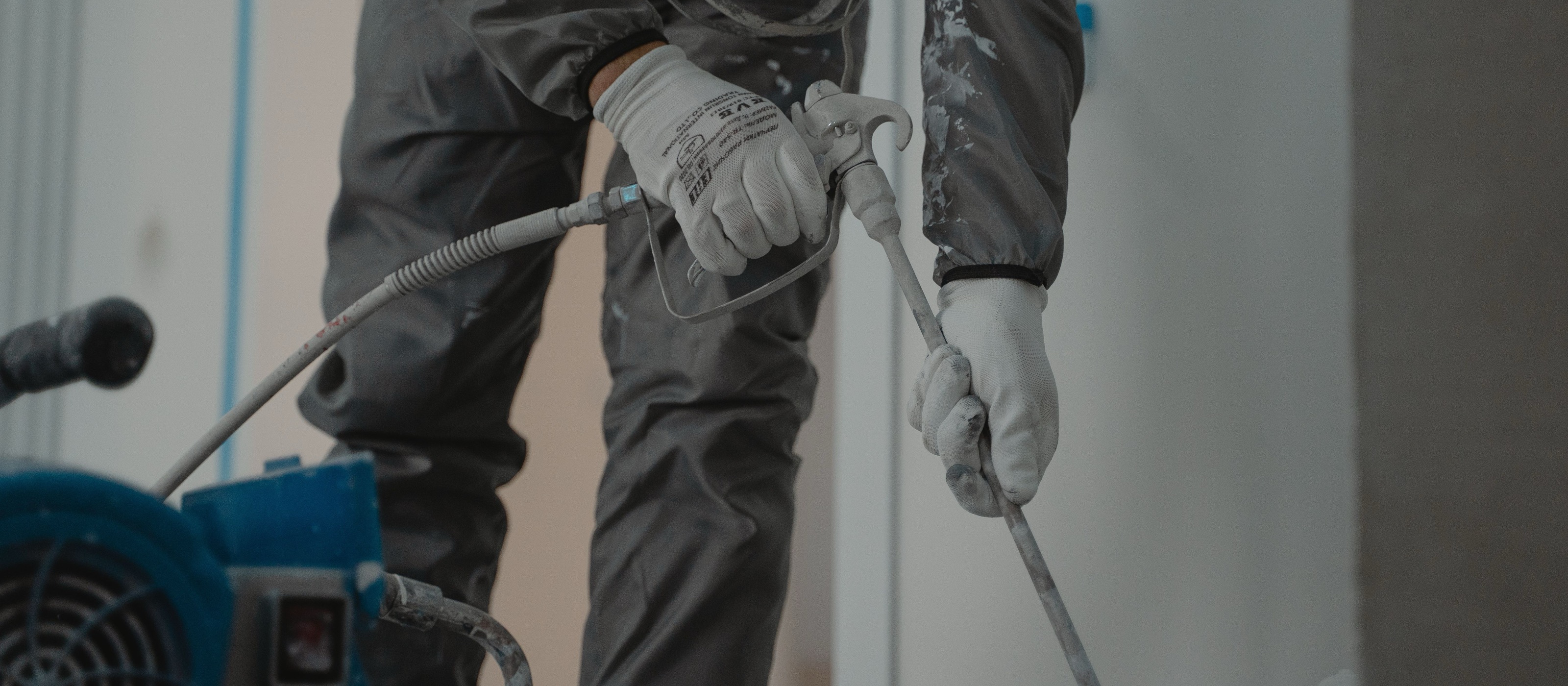 Operator in protective gear and respirator handling a spray gun connected to a professional spray rig