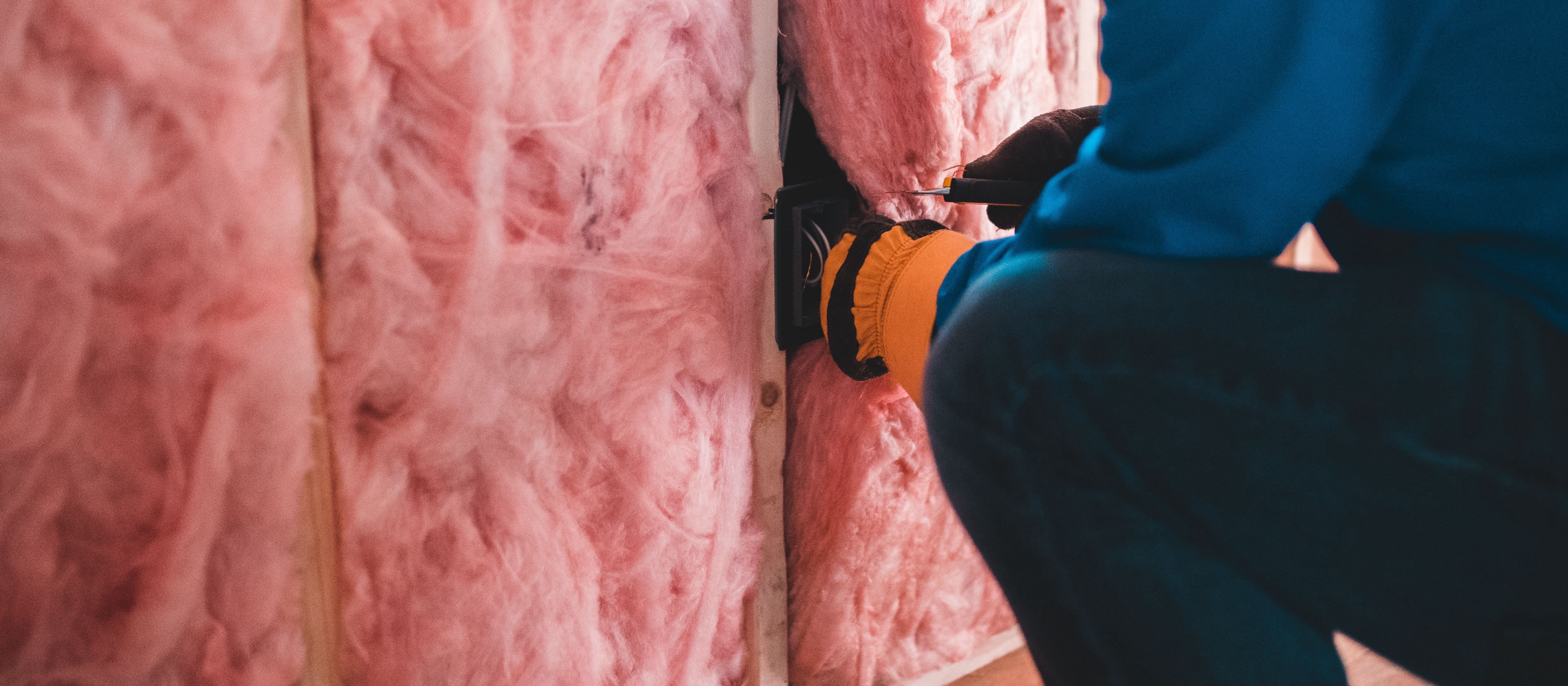 Worker installing mineral wool thermal insulation between timber studs of a framed wall