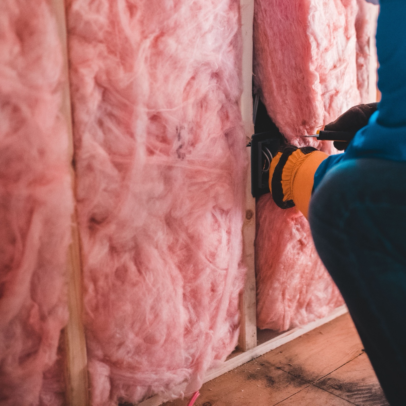 Worker fitting mineral wool insulation between timber wall studs